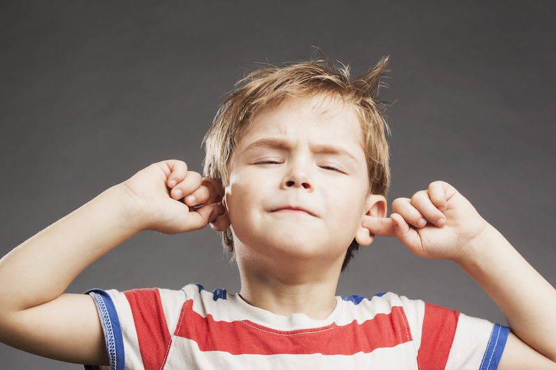 Young boy covering ears against gray background