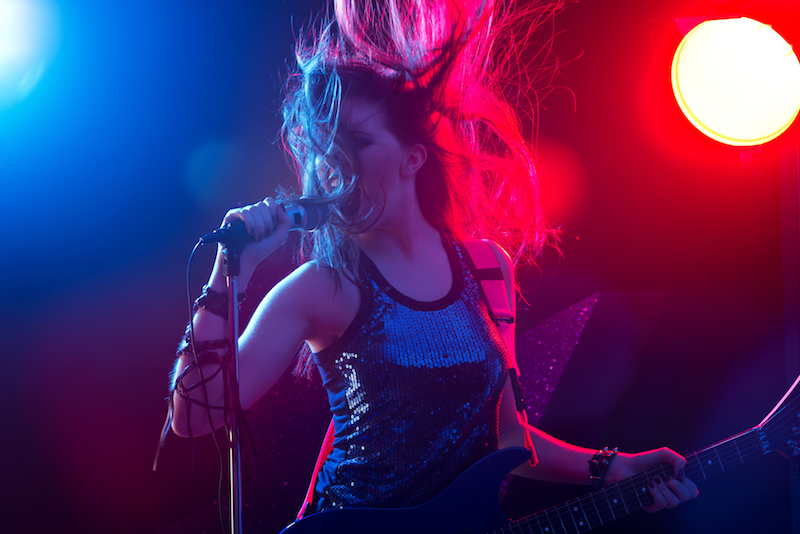 Young rock star singing with stage lights on background.